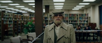 Movie still from “American Animals” (2018), directed by Bart Layton – An older man wearing a hat in a library; Medium shot, High angle