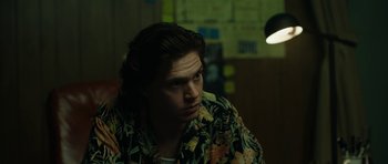 Movie still from “American Animals” (2018), directed by Bart Layton – A man with long brown hair wearing a floral shirt; Medium shot, Over the shoulder angle