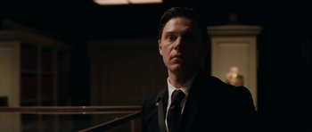 Movie still from “American Animals” (2018), directed by Bart Layton – A man wearing a suit and tie standing in a room; Close Up shot, Low angle