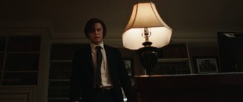 Movie still from “American Animals” (2018), directed by Bart Layton – A man standing in front of a lamp in a dark room; Medium shot, Low angle