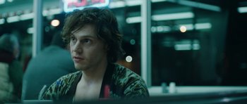 Movie still from “American Animals” (2018), directed by Bart Layton – A man sitting at a table in front of a neon sign; Close Up shot, Low angle