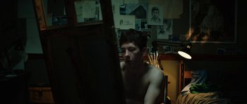 Movie still from “American Animals” (2018), directed by Bart Layton – A man sitting in front of an easel in a room; Medium shot, High angle