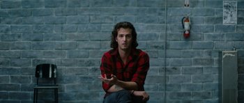 Movie still from “American Animals” (2018), directed by Bart Layton – A man sitting on the ground in front of a brick wall; Close Up shot, Over the shoulder angle