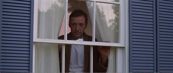 Movie still from “American Beauty” (1999), directed by Sam Mendes – A man looking out of a window through a curtain; Medium shot, Low angle