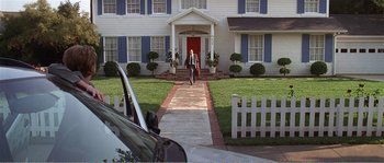 Movie still from “American Beauty” (1999), directed by Sam Mendes – A man walking down a sidewalk in front of a house; Extreme Wide shot, High angle