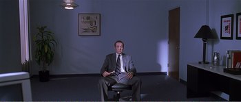 Movie still from “American Beauty” (1999), directed by Sam Mendes – A man in a suit and tie sitting on top of a chair; Wide shot, High angle