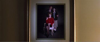 Movie still from “American Beauty” (1999), directed by Sam Mendes – A picture of two people and a man sitting on a chair; Medium shot, High angle