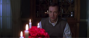 Movie still from “American Beauty” (1999), directed by Sam Mendes – A man sitting in front of a table with roses and lit candles; Close Up shot, Over the shoulder angle