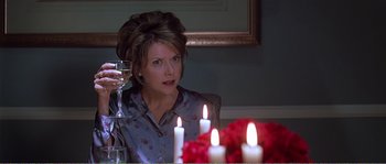 Movie still from “American Beauty” (1999), directed by Sam Mendes – A woman sitting at a table holding a wine glass; Close Up shot, Over the shoulder angle