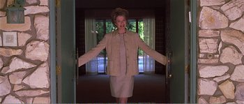 Movie still from “American Beauty” (1999), directed by Sam Mendes – A woman in a white dress and a beige jacket is standing in a doorway; Medium shot, Low angle