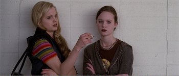 Movie still from “American Beauty” (1999), directed by Sam Mendes – A woman smoking a cigarette next to another woman in front of a brick wall; Medium shot, Over the shoulder angle