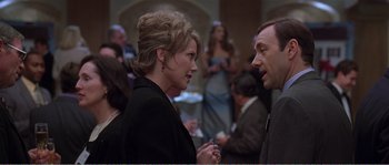 Movie still from “American Beauty” (1999), directed by Sam Mendes – A woman and a man talking to each other in front of a crowd; Medium shot, Over the shoulder angle