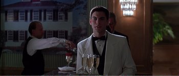Movie still from “American Beauty” (1999), directed by Sam Mendes – A man in a white tuxedo sitting at a table with champagne flutes in front of him; Medium shot, Low angle