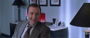 Movie still from “American Beauty” (1999), directed by Sam Mendes – A man wearing a suit and tie smiling for the camera; Close Up shot, Over the shoulder angle