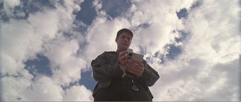 Movie still from “American Beauty” (1999), directed by Sam Mendes – A man holding a camera in front of a cloudy sky; Medium shot, Low angle