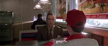 Movie still from “American Beauty” (1999), directed by Sam Mendes – A man sitting at a table in front of another man; Medium shot, Over the shoulder angle