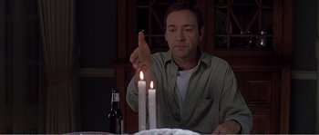 Movie still from “American Beauty” (1999), directed by Sam Mendes – A man sitting at a table with a lit candle in front of him; Medium shot, Over the shoulder angle