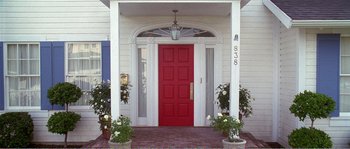 Movie still from “American Beauty” (1999), directed by Sam Mendes – A red front door of a white house with potted plants; Wide shot, High angle