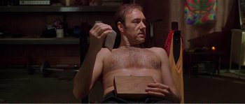 Movie still from “American Beauty” (1999), directed by Sam Mendes – A man sitting in a chair holding a knife and a box; Medium shot, Low angle