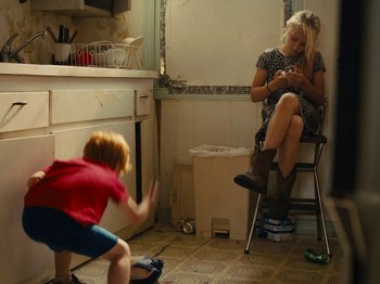 Movie still from “American Honey” (2016), directed by Andrea Arnold – A young boy and a woman in a kitchen; Wide shot, High angle