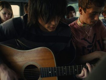 Movie still from “American Honey” (2016), directed by Andrea Arnold – Two young men are playing a guitar in a bus; Medium shot, Over the shoulder angle