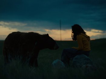 Movie still from “American Honey” (2016), directed by Andrea Arnold – A woman sitting in a field next to a brown bear; Wide shot, Low angle
