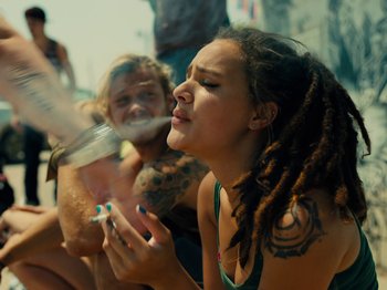 Movie still from “American Honey” (2016), directed by Andrea Arnold – A woman with dreadlocks is smoking a cigarette; Medium shot, High angle