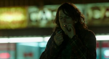 Movie still from “American Ultra” (2015), directed by Nima Nourizadeh – A woman smoking a cigarette while looking at her cell phone; Medium shot, Over the shoulder angle