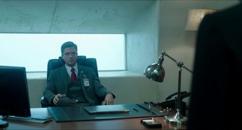 Movie still from “American Ultra” (2015), directed by Nima Nourizadeh – A man sitting at a desk in front of a lamp; Medium shot, Low angle