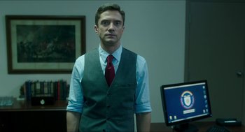 Movie still from “American Ultra” (2015), directed by Nima Nourizadeh – A man wearing a vest and a red tie standing in front of a computer; Medium shot, Over the shoulder angle