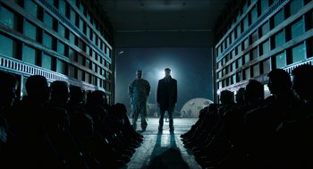 Movie still from “American Ultra” (2015), directed by Nima Nourizadeh – Two men standing in front of a group of people in a building; Wide shot, Low angle