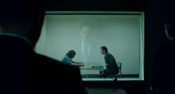 Movie still from “American Ultra” (2015), directed by Nima Nourizadeh – Two men sitting at a table in front of a projection screen; Medium shot, Over the shoulder angle