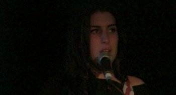 Movie still from “Amy” (2015), directed by Asif Kapadia – A woman with long dark hair is holding a microphone; Close Up shot, High angle
