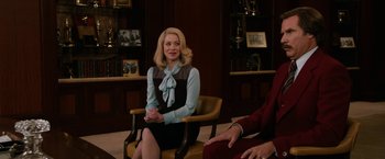 Movie still from “Anchorman 2: The Legend Continues” (2013), directed by Adam McKay – A woman sitting on a chair in a room; Medium shot, Over the shoulder angle