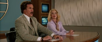 Movie still from “Anchorman 2: The Legend Continues” (2013), directed by Adam McKay – A man and a woman sitting in front of a news desk; Medium shot, Low angle