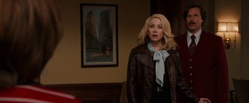 Movie still from “Anchorman 2: The Legend Continues” (2013), directed by Adam McKay – A woman standing in front of a painting in a room; Medium shot, Over the shoulder angle