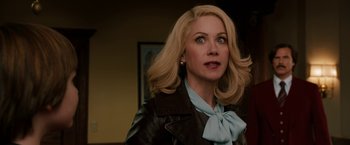 Movie still from “Anchorman 2: The Legend Continues” (2013), directed by Adam McKay – A woman with blonde hair wearing a leather jacket and a blue bow tie; Close Up shot, Over the shoulder angle