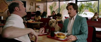 Movie still from “Anchorman 2: The Legend Continues” (2013), directed by Adam McKay – A man sitting at a table in front of a bowl of food; Medium shot, Over the shoulder angle