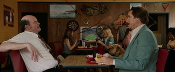 Movie still from “Anchorman 2: The Legend Continues” (2013), directed by Adam McKay – A group of people sitting at a table eating food; Medium shot, Over the shoulder angle