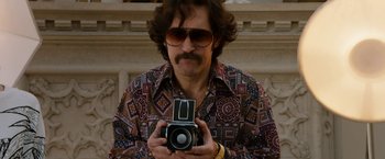 Movie still from “Anchorman 2: The Legend Continues” (2013), directed by Adam McKay – A man holding a camera while wearing sunglasses; Medium shot, Low angle