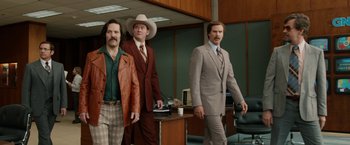 Movie still from “Anchorman 2: The Legend Continues” (2013), directed by Adam McKay – A group of men standing next to each other in a room; Wide shot, Low angle