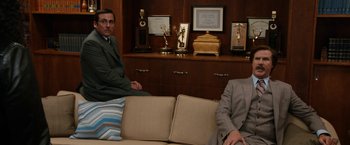 Movie still from “Anchorman 2: The Legend Continues” (2013), directed by Adam McKay – Two men sitting on a couch in front of a trophy case; Wide shot, High angle