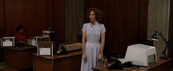 Movie still from “Anchorman 2: The Legend Continues” (2013), directed by Adam McKay – A woman standing in front of a desk in an office; Medium shot, Over the shoulder angle