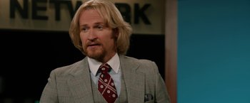 Movie still from “Anchorman 2: The Legend Continues” (2013), directed by Adam McKay – A man with long blonde hair wearing a suit and tie; Close Up shot, Over the shoulder angle