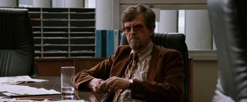 Movie still from “Anchorman 2: The Legend Continues” (2013), directed by Adam McKay – An older man sitting at a desk in a room; Medium shot, Over the shoulder angle