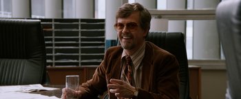 Movie still from “Anchorman 2: The Legend Continues” (2013), directed by Adam McKay – An older man sitting at a table with a glass of water; Medium shot, Over the shoulder angle