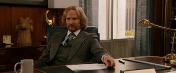 Movie still from “Anchorman 2: The Legend Continues” (2013), directed by Adam McKay – A man sitting at a desk in front of a window; Medium shot, Over the shoulder angle