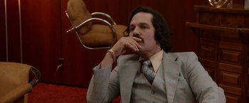 Movie still from “Anchorman 2: The Legend Continues” (2013), directed by Adam McKay – A man in a suit and tie sitting in front of a chair; Close Up shot, Low angle