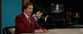 Movie still from “Anchorman 2: The Legend Continues” (2013), directed by Adam McKay – Anchorman ron burgundy sitting in front of a television; Medium shot, Over the shoulder angle