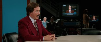 Movie still from “Anchorman 2: The Legend Continues” (2013), directed by Adam McKay – Anchorman ron burgandy sitting in front of a television; Medium shot, Over the shoulder angle